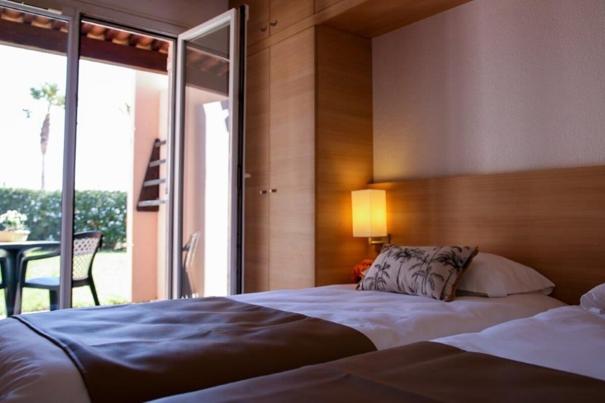 A hotel room with a bed, a nightstand with a lamp, and a sliding glass door leading to an outdoor area.