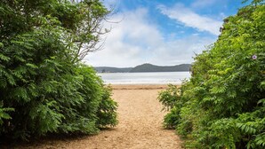 Un sendero arenoso que lleva a una playa con vistas al mar y colinas distantes.