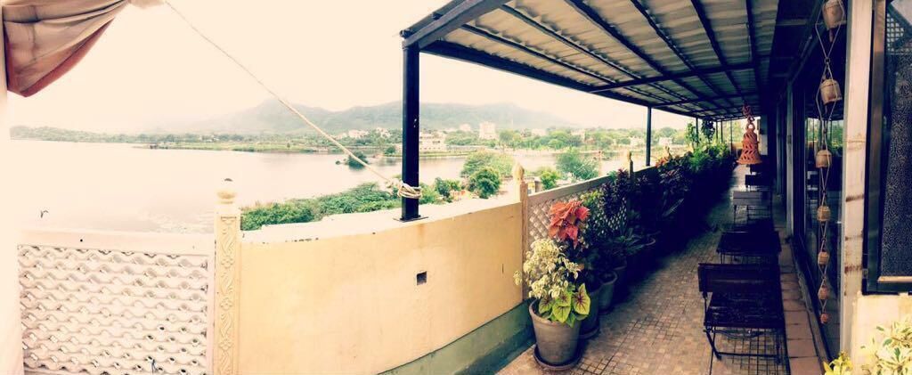 A covered outdoor area with a view of a river and mountains, potted plants, and outdoor seating.
