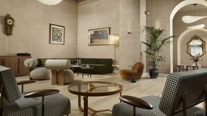 Uma sala de estar espaçosa com um sofá verde, cadeiras estampadas em xadrez, uma mesa de centro de vidro e uma grande planta em vaso.