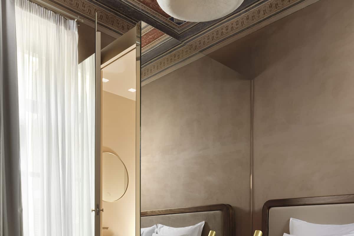 Quarto moderno com uma cama grande, mesa de cabeceira com abajur e vista para um banheiro.