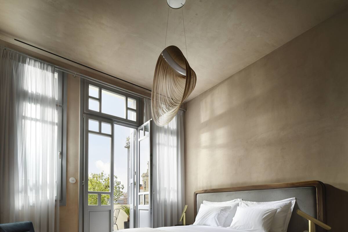 Quarto moderno com uma cama grande, uma cadeira, uma mesinha de cabeceira e vista através de uma porta aberta.