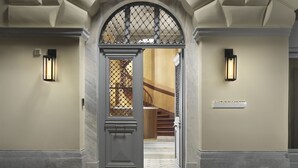 Entrada de hotel com um arco imponente, escadaria que leva para o interior e duas luminárias fixadas na parede.