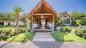 A resort with a thatched-roof structure, a paved pathway leading to it, and a well-maintained garden with palm trees and shrubs.