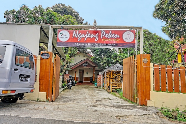 A gated entrance to a property named 'Ngajeng Peken Home Stay' with a signboard, a parked car, and a motorcycle. - Ngajeng Peken Home Stay (Batu)