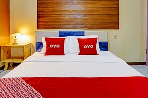 A hotel room with a bed, two pillows with the word 'OYO' on them, a nightstand with a lamp, and a wooden headboard. - Ngajeng Peken Home Stay (Batu)