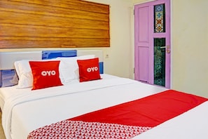 A hotel room with a bed, pillows with 'OYO' branding, a wooden headboard, and a purple door with a decorative window. - Ngajeng Peken Home Stay (Batu)