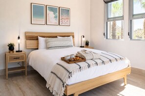 Un dormitorio con una cama de madera, mesitas de noche y una ventana con vista a palmeras.