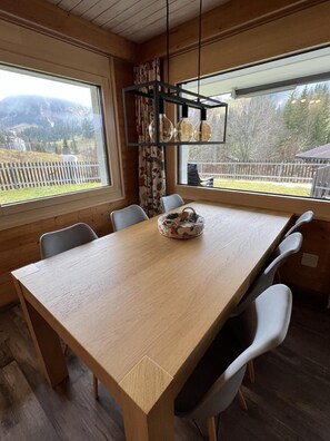 Enjoy meals in this dining area with a long table and six chairs, surrounded by large windows offering a view of the mountains.