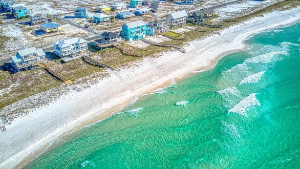 An aerial view of a coastal residential area with houses along the beach, clear turquoise waters, and a sandy shoreline. - Coastal Camphouse: Gulf View Home | Private Pool, Pet Friendly, Amenities+ (Navarre)