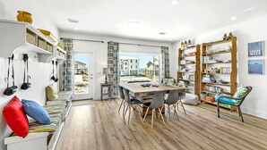 A modern interior with a dining area, bookshelves, and a bench with colorful cushions. - Coastal Camphouse: Gulf View Home | Private Pool, Pet Friendly, Amenities+ (Navarre)