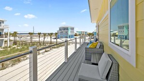 A balcony with a view of the beach, a wicker sofa, and a railing. - Coastal Camphouse: Gulf View Home | Private Pool, Pet Friendly, Amenities+ (Navarre)