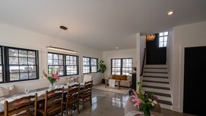A spacious dining area with a long wooden table and chairs, large windows, and a staircase. - Luxury Douglas Beach House (Douglas)