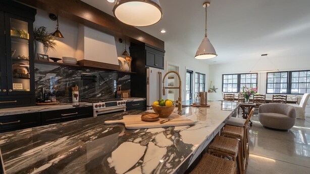 A modern kitchen with a marble countertop, dark cabinetry, and a dining area with wicker furniture. - Luxury Douglas Beach House (Douglas)