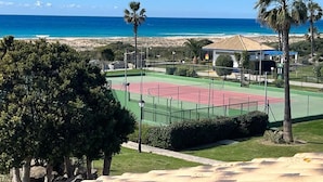A tennis court with a beach view, surrounded by palm trees and a building with a red roof. - Endless Summer Beach House, Atlanterra (AN)
