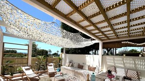 A covered outdoor seating area with wicker furniture, a table with a bottle and glasses, and a view of the sea. - Endless Summer Beach House, Atlanterra (AN)