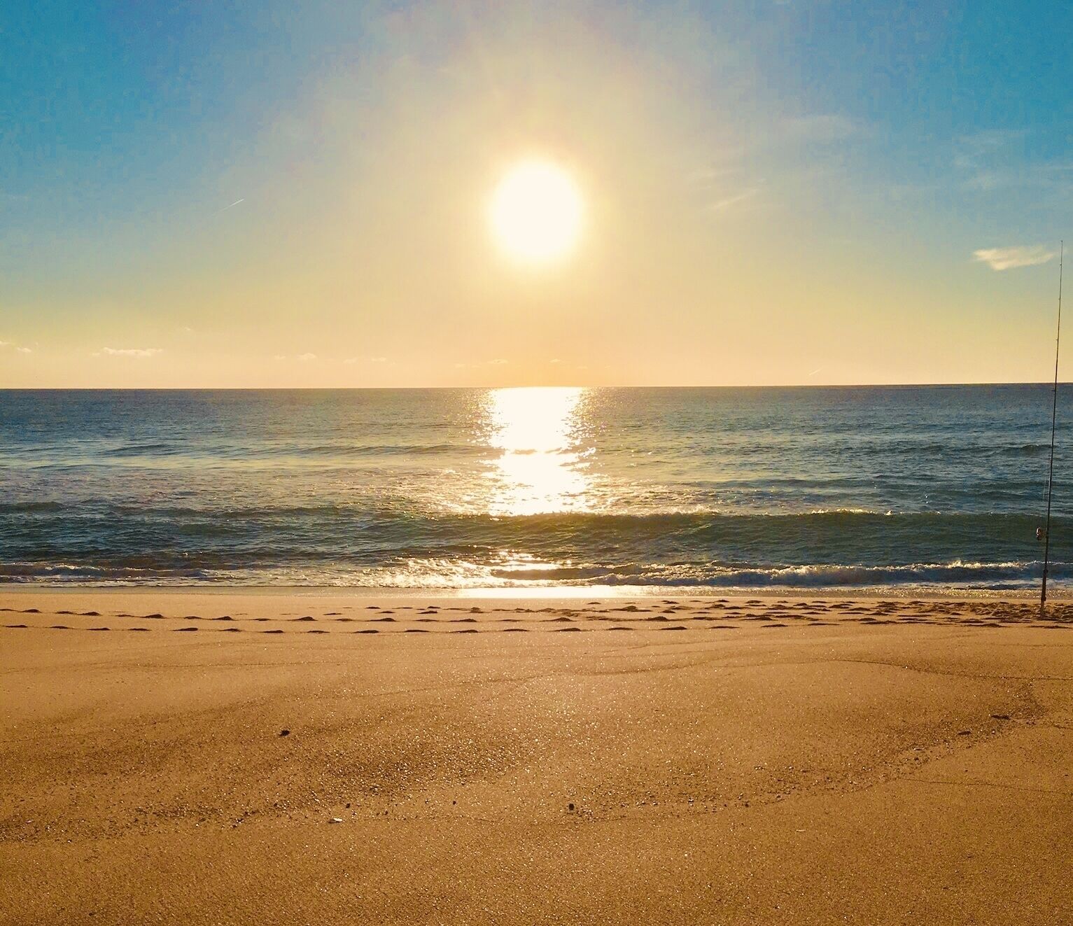 Une plage avec un ciel dégagé et le soleil se reflétant sur l’eau.