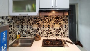 Una cocina con armarios blancos, salpicadero de azulejos, pileta de acero inoxidable y estufa a gas.