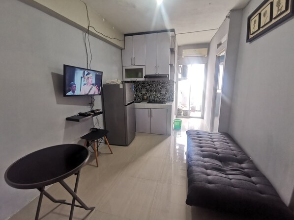A compact living space with a kitchenette, a dining area with a chair and a sofa, and a TV mounted on the wall.