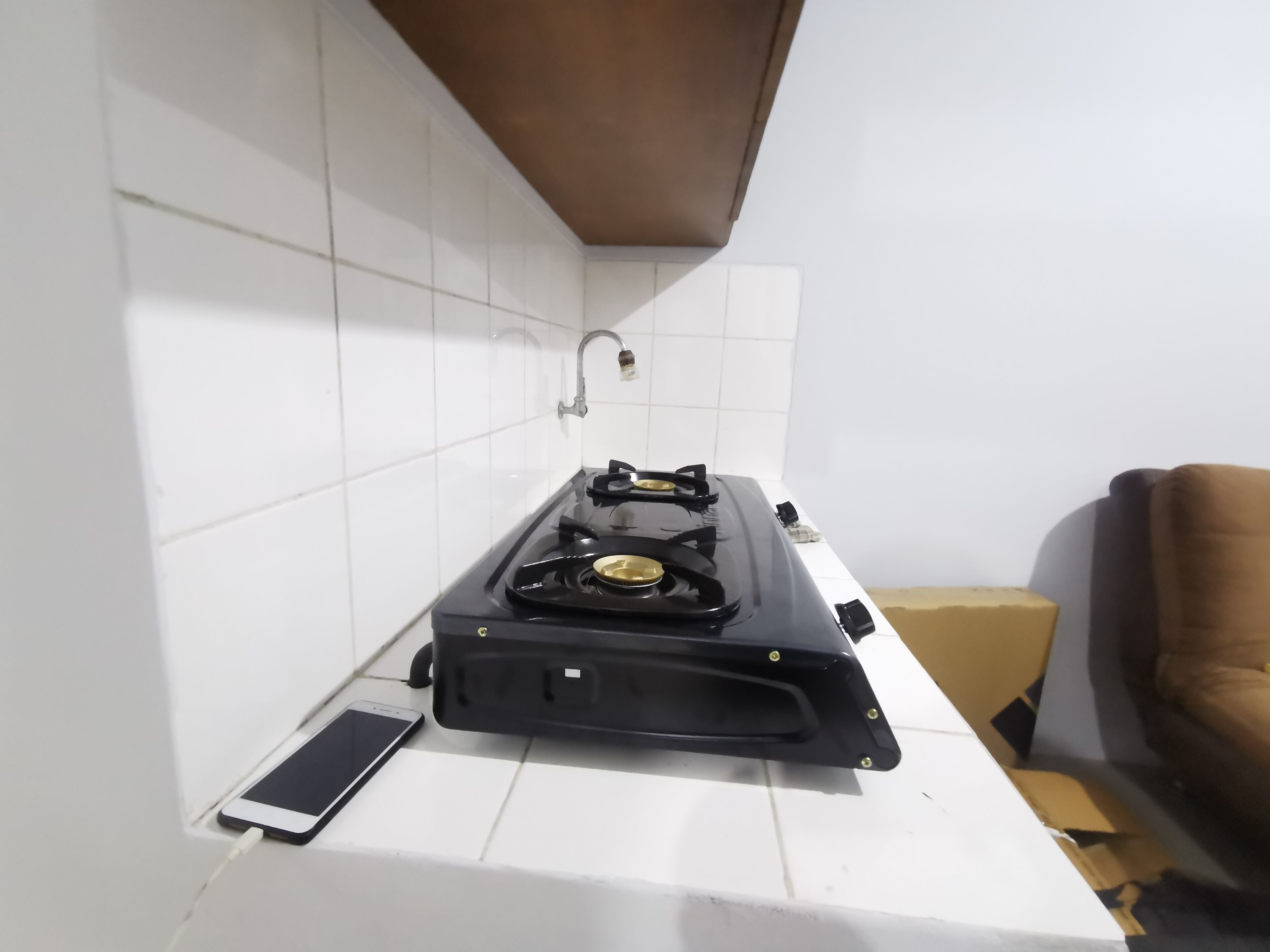 A kitchen with white tiled walls, a gas stove, and a smartphone charging on the counter.