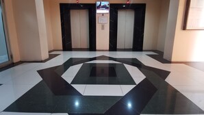 Un hall con suelo de estampado geométrico, dos ascensores y un televisor instalado en la pared.