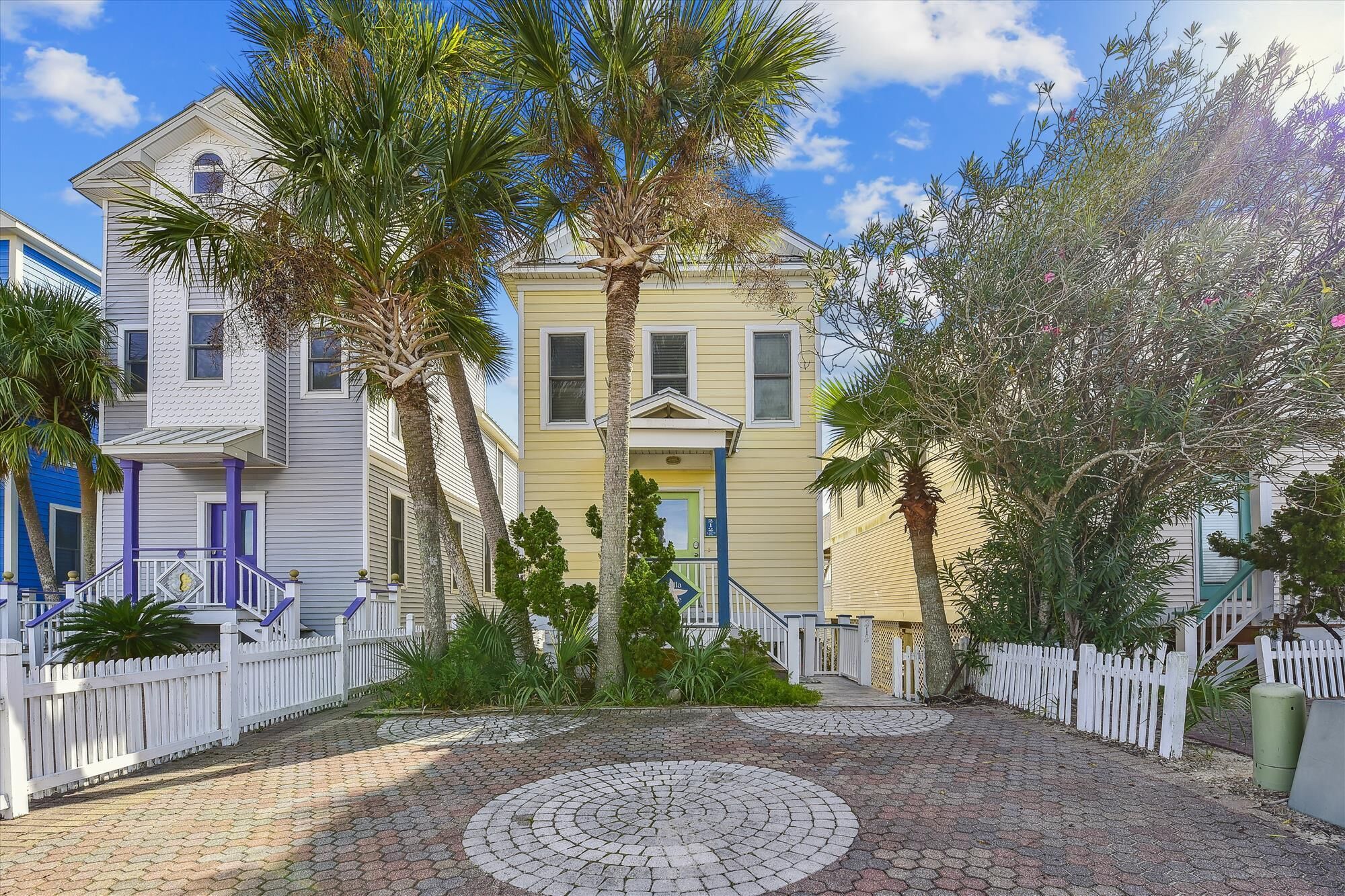 A courtyard with a paved circular area, surrounded by a white picket fence, and houses with balconies and windows.