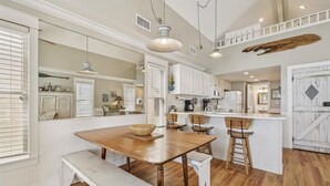 A kitchen with a wooden dining table, white cabinets, and a hanging light fixture. - Welcome to Stella Di Mare! (St. George Island)