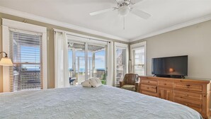 A bedroom with a large bed, a television, a wooden dresser, and a balcony with a view of the ocean. - Welcome to Stella Di Mare! (St. George Island)