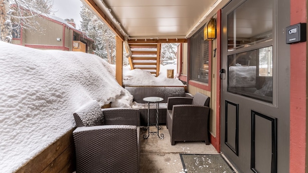 A covered outdoor seating area with wicker furniture and a small table, a door with a window, and snow-covered surroundings. - Close to Main Street, Access to Nearby Ski Resorts; Private Patio! (Frisco)