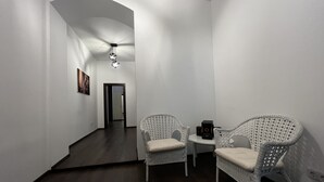 A hallway with two wicker chairs and a small table, a ceiling light, and a door at the end. - Old City Appartment (București)