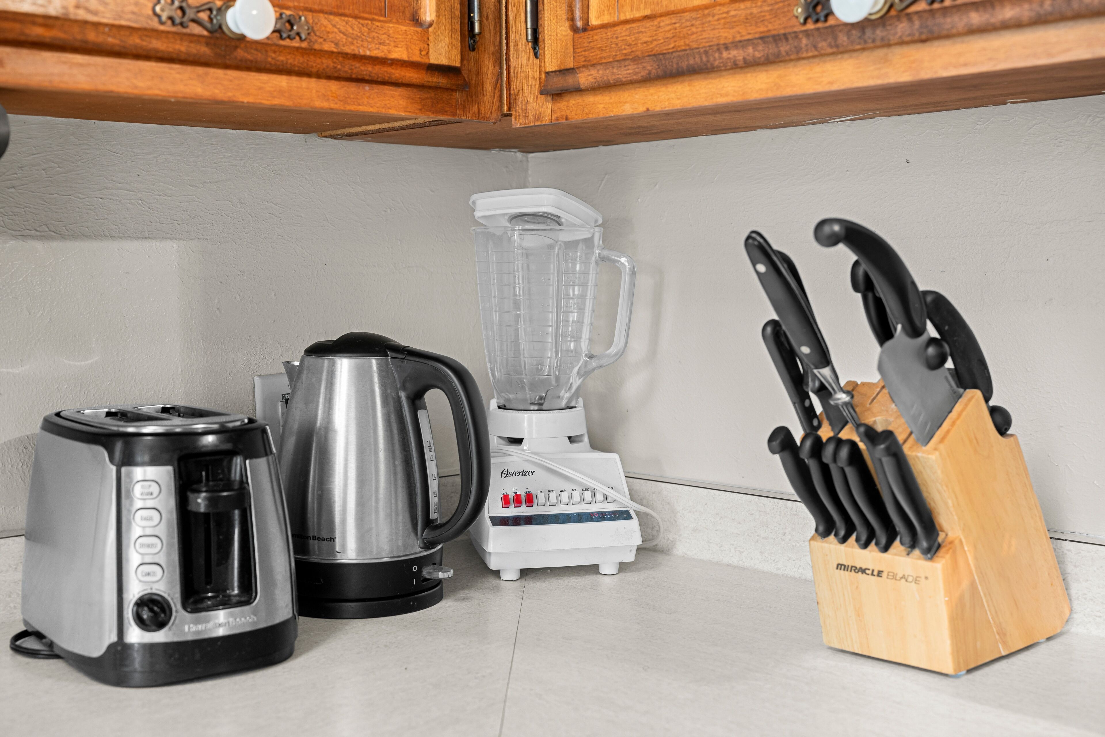 A kitchen with a toaster, a blender, a kettle, and a knife block.