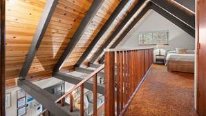 Un dormitorio en ático con techos altos, vigas de madera a la vista, suelo alfombrado, cama y mesita de noche.