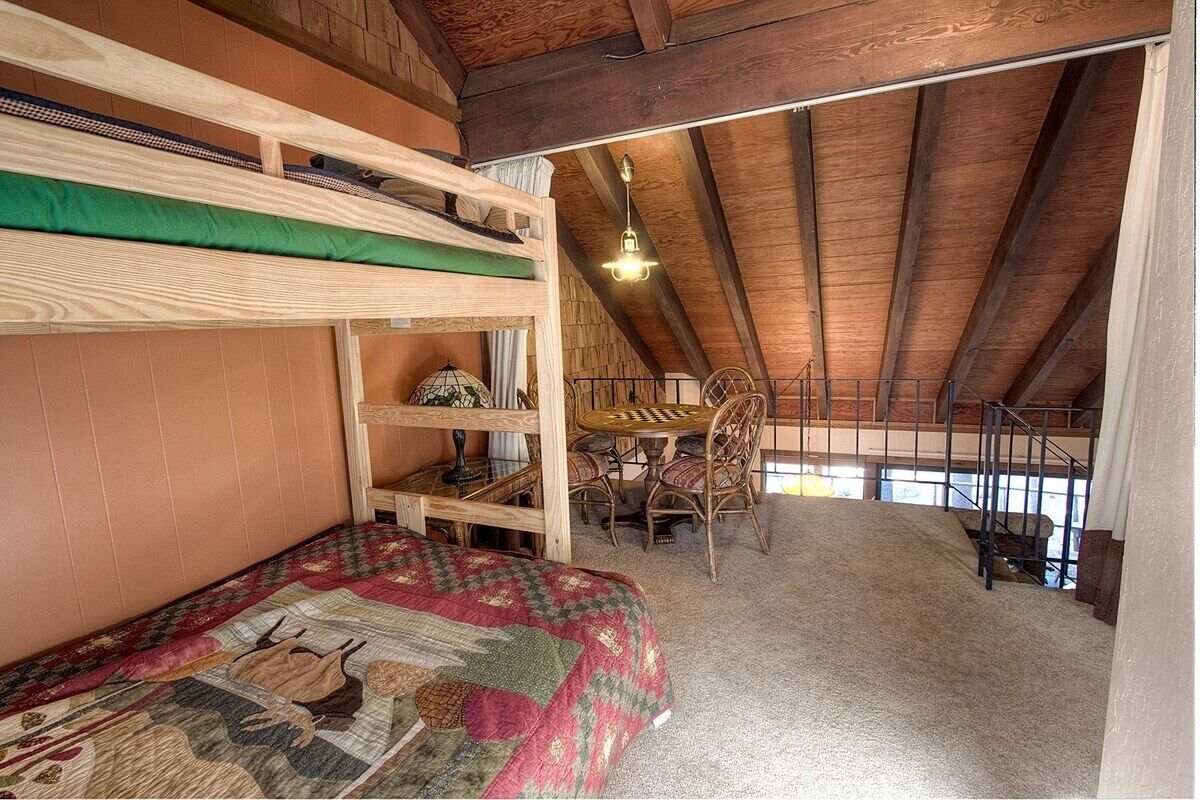 Une chambre de style « loft » avec un lit superposé, une table à manger avec des chaises et une vue sur l’extérieur.