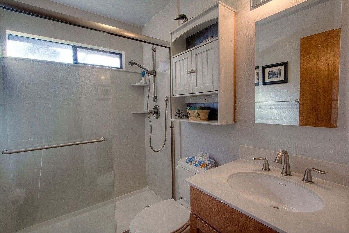 A modern bathroom with a glass-enclosed shower, a white sink with two faucets, and a wooden vanity.