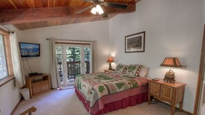 A bedroom with a bed, two bedside tables, a ceiling fan, a television, and a window with a view of trees. - Bear Country 4 Bedroom Home by RedAwning (South Lake Tahoe)