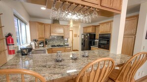 A kitchen with wooden cabinets, granite countertops, and a central island with chairs. - Bear Country 4 Bedroom Home by RedAwning (South Lake Tahoe)