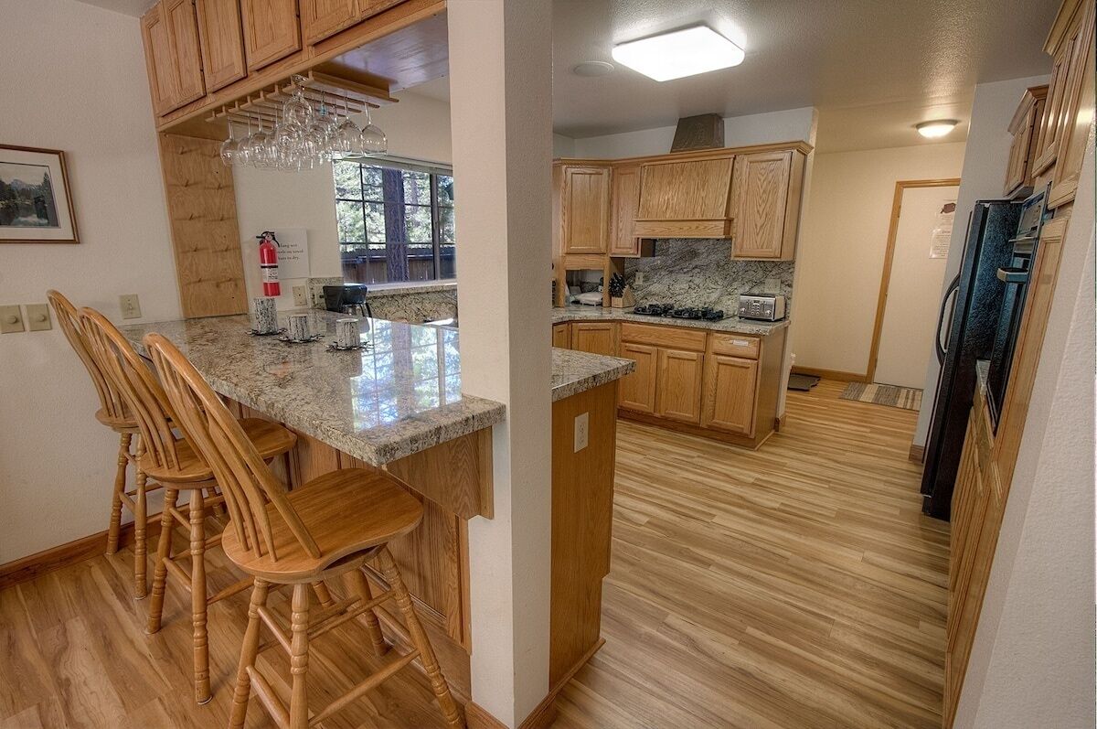 Una cocina con gabinetes de madera, encimeras de granito y una isla central con taburetes de bar.