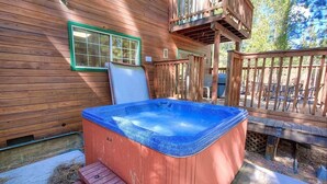 A wooden deck with a hot tub, a wooden deck chair, and a wooden deck with a view of the surrounding trees. - Bear Country 4 Bedroom Home by RedAwning (South Lake Tahoe)