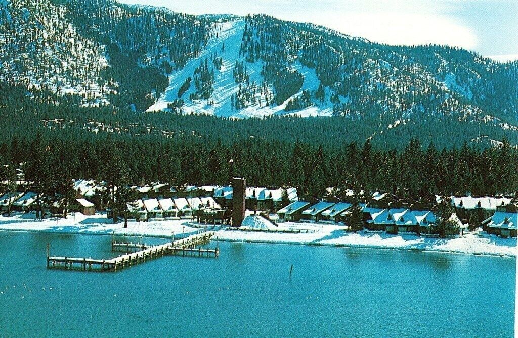 Uma montanha coberta de neve com uma fileira de cabanas à beira de um lago.