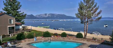 Área de piscina com vista para o mar e montanhas, cadeiras de descanso e um edifício com varanda.
