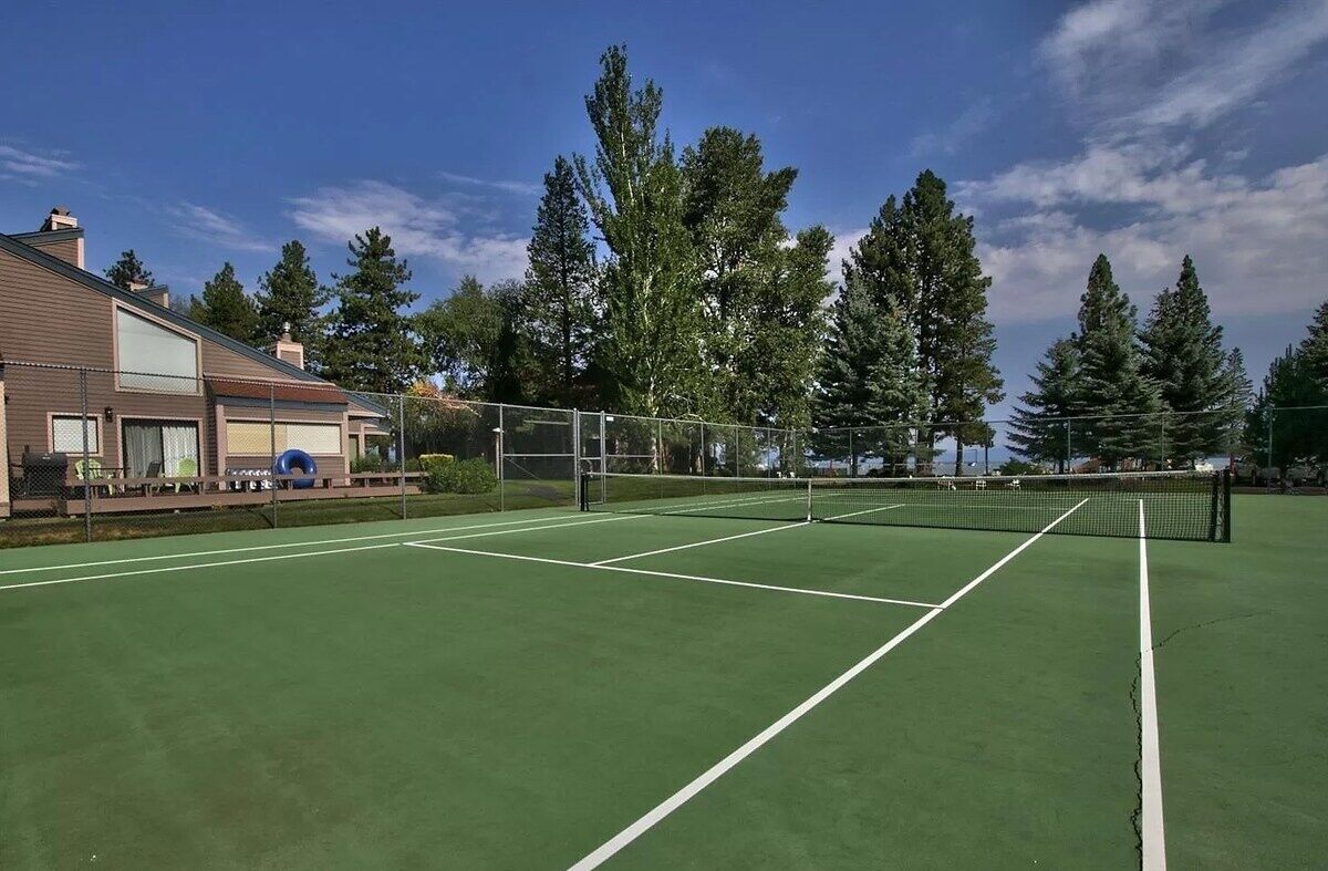 Een tennisbaan met een net, omringd door bomen en een gebouw.