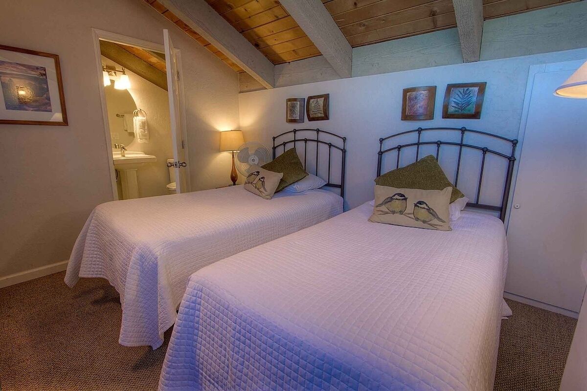 Ein Schlafzimmer mit zwei Einzelbetten, einer Holzbalkendecke und einem durch eine geöffnete Tür einsehbaren Badezimmer.