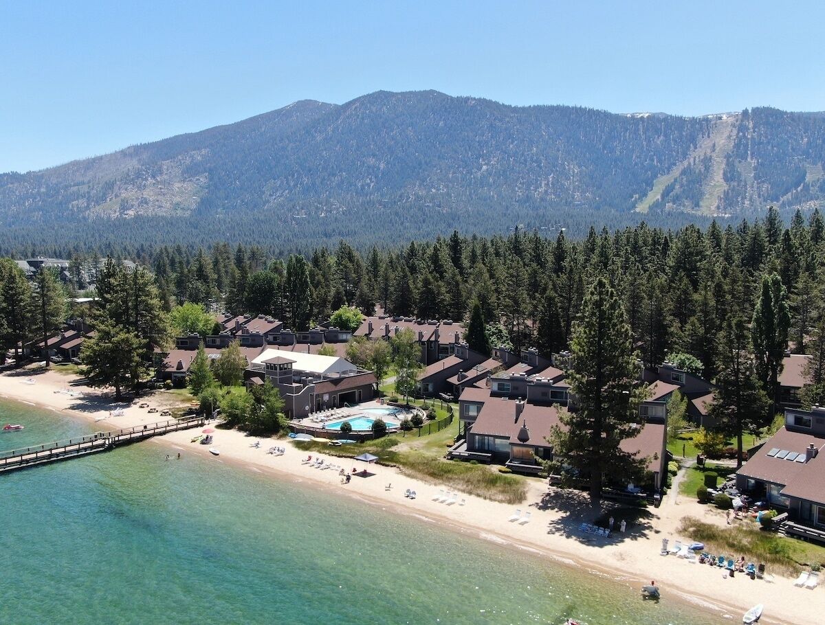 An aerial view of a coastal resort with multiple cabins, a swimming pool, and a beach.