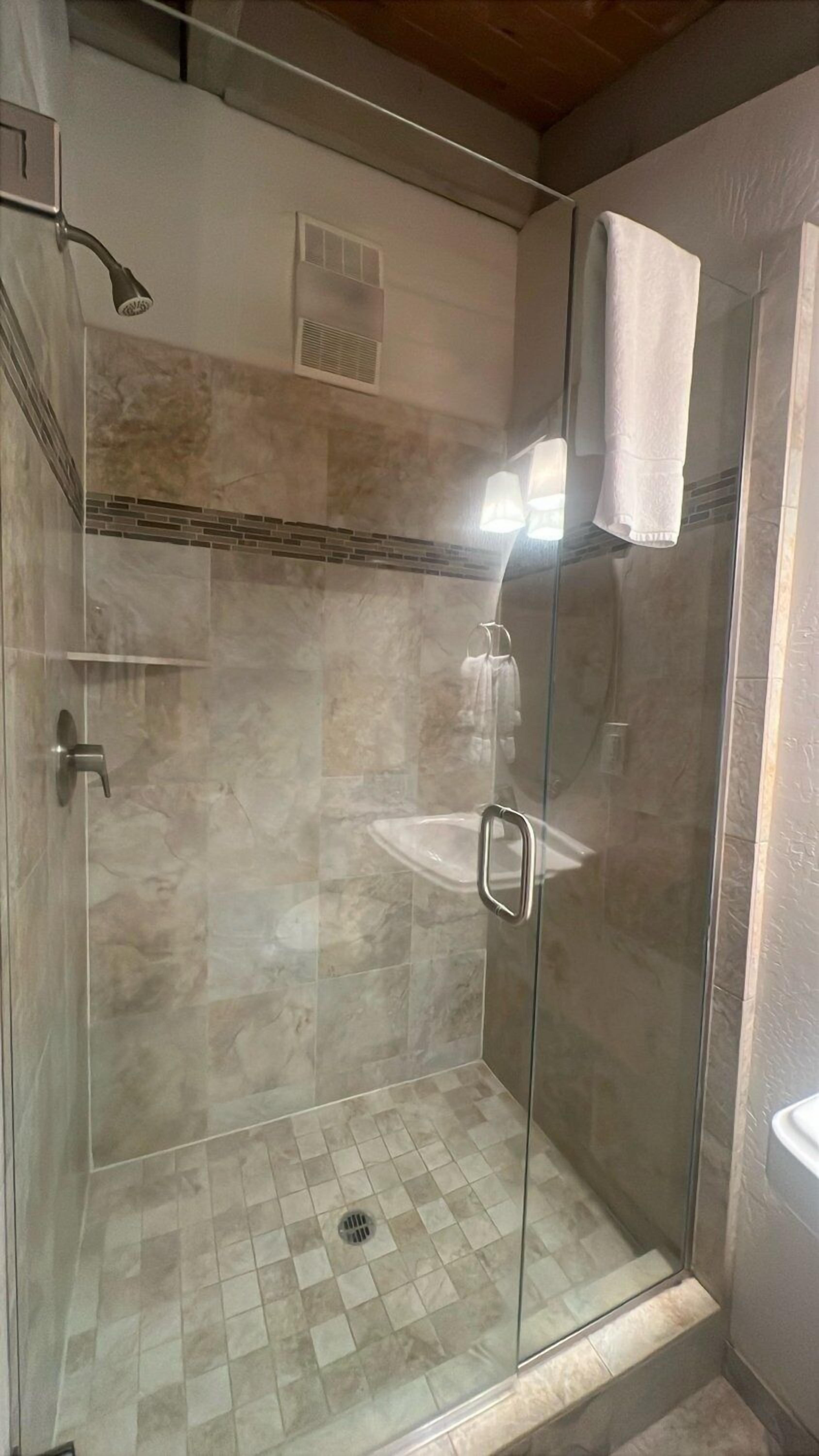 A glass-enclosed shower with a tiled floor and a bench.