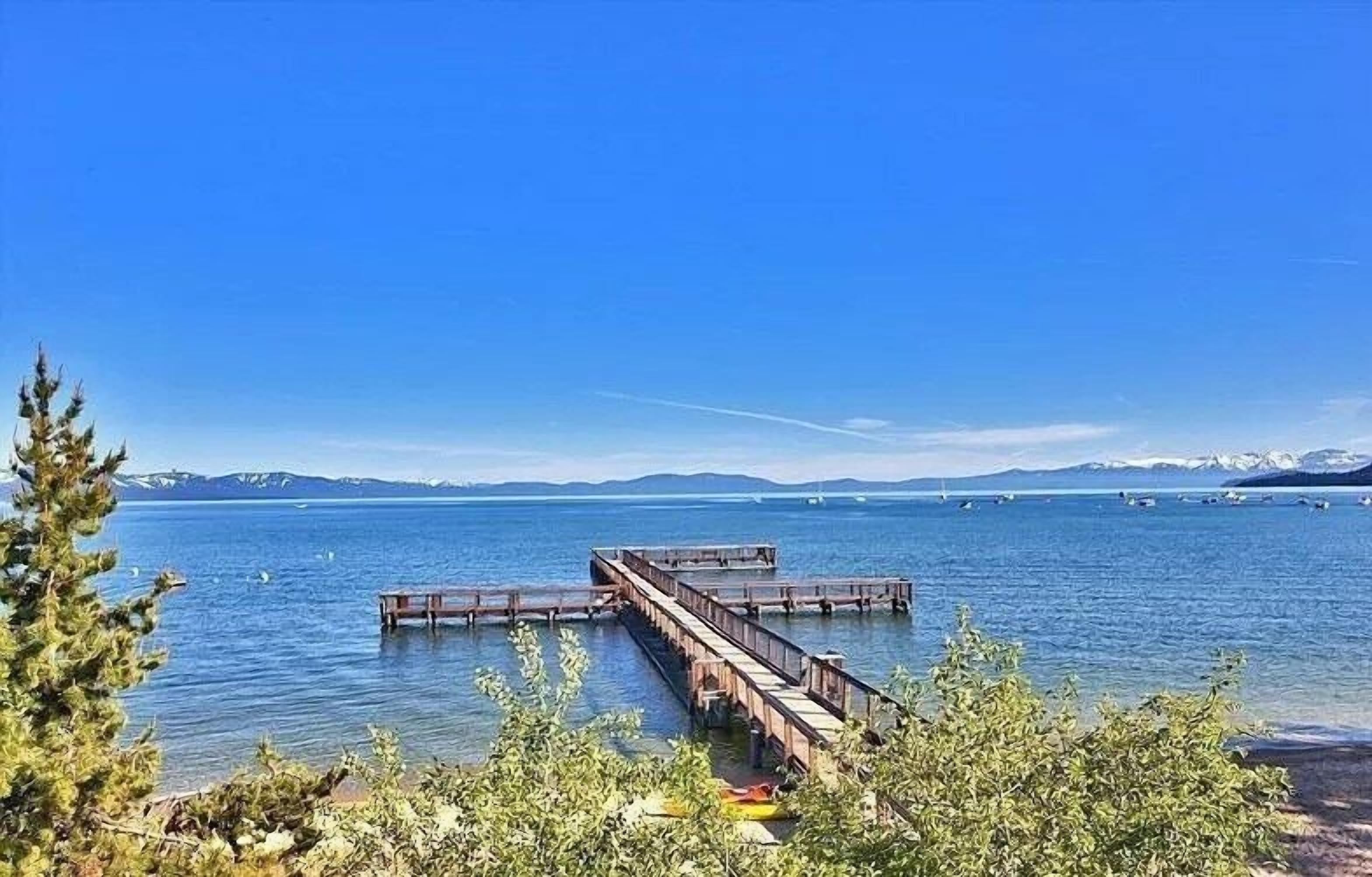 A clear view of a lake with a wooden pier extending into the water, surrounded by greenery and mountains in the background.