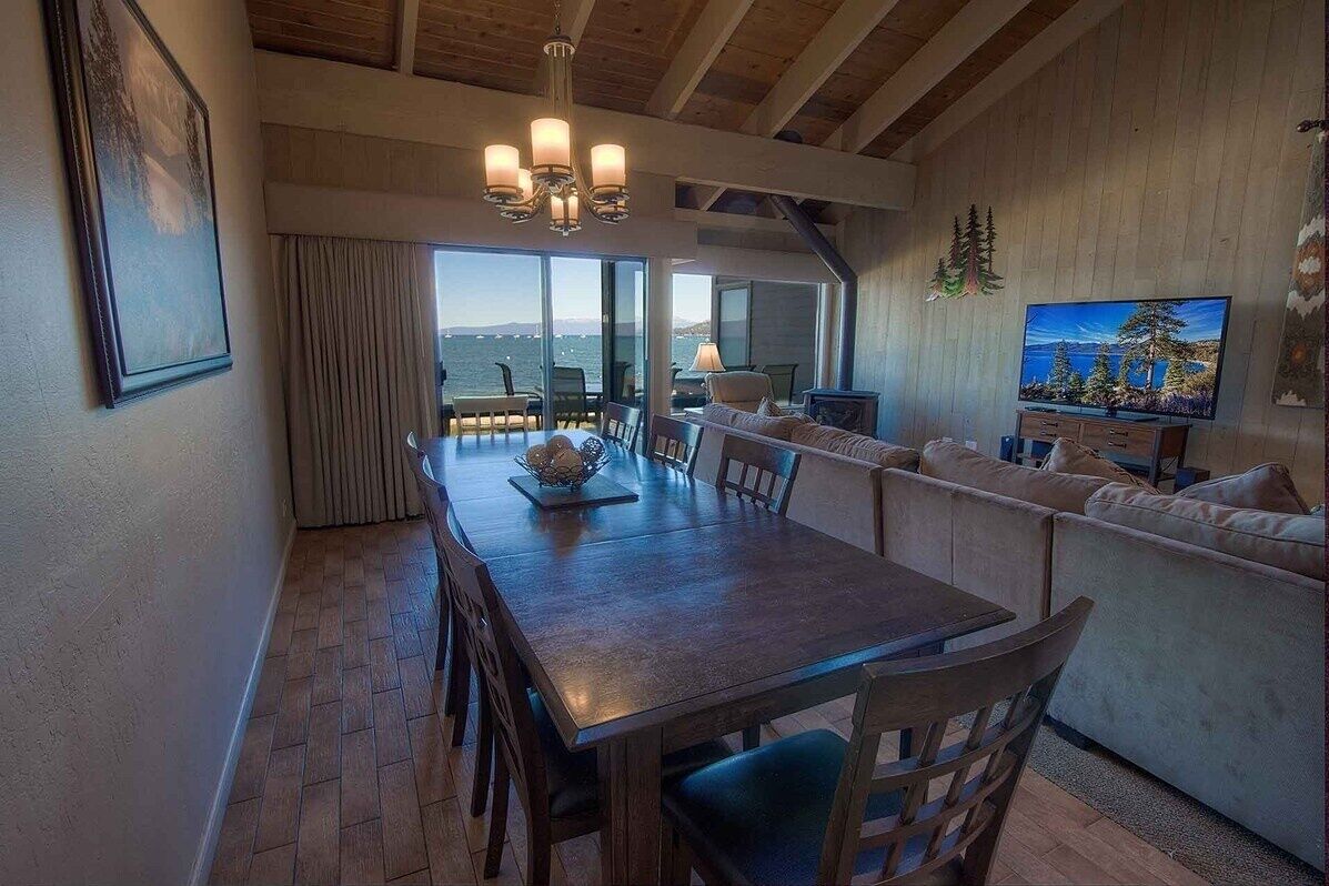 Uma sala de jantar com mesa e cadeiras de madeira, um candelabro, um sofá e uma televisão.