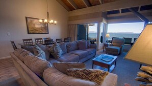 A living room with a sofa set, a coffee table, and a dining area with chairs and a table. There is a large window with a view of the sea. - Sky Lake Splendor 5 Bedroom Condo by RedAwning (South Lake Tahoe)