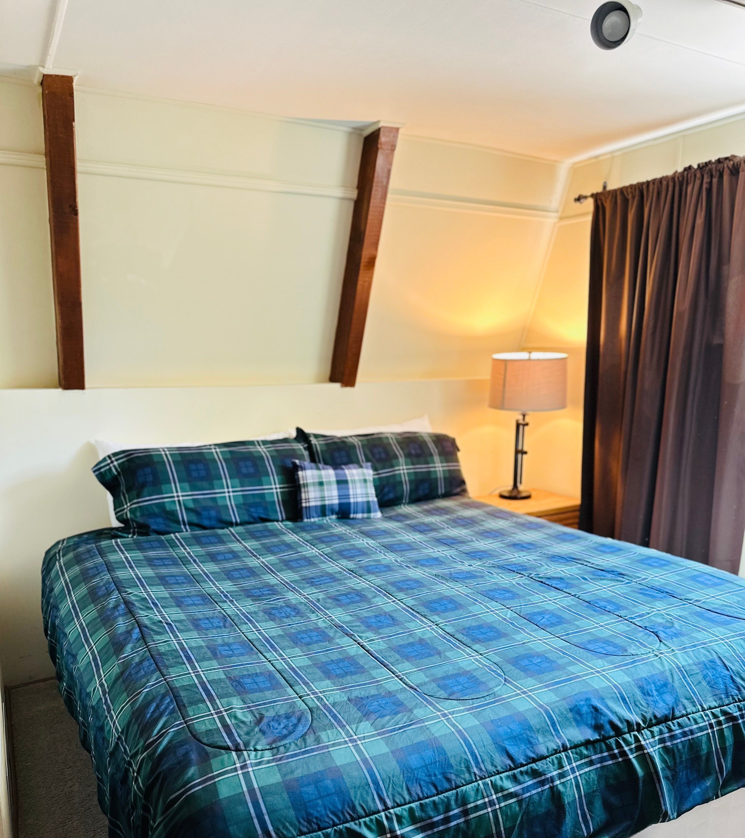 A hotel room with a bed, a nightstand, a lamp, and a window with curtains.