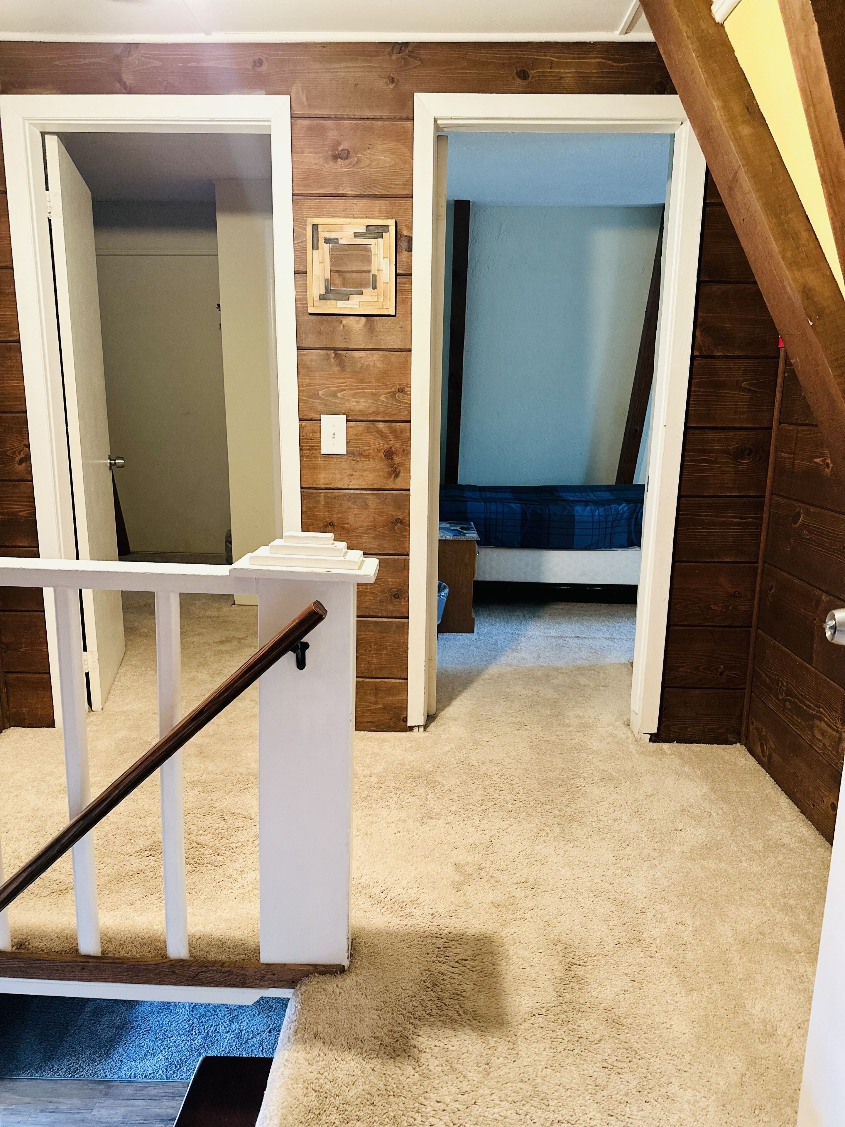 Un escalier menant à une chambre à coucher avec une couvre-lit bleue, un mur en bois et un plancher recouvert de moquette.