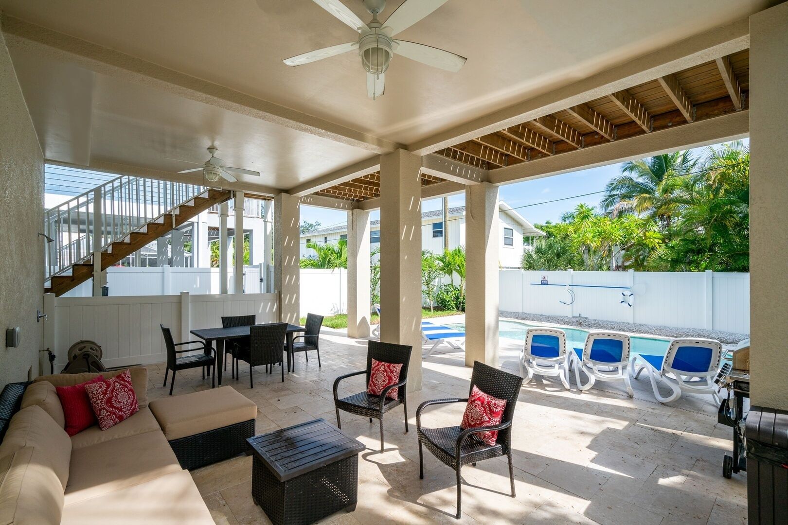 A covered outdoor area with a pool, lounge chairs, and a dining table.